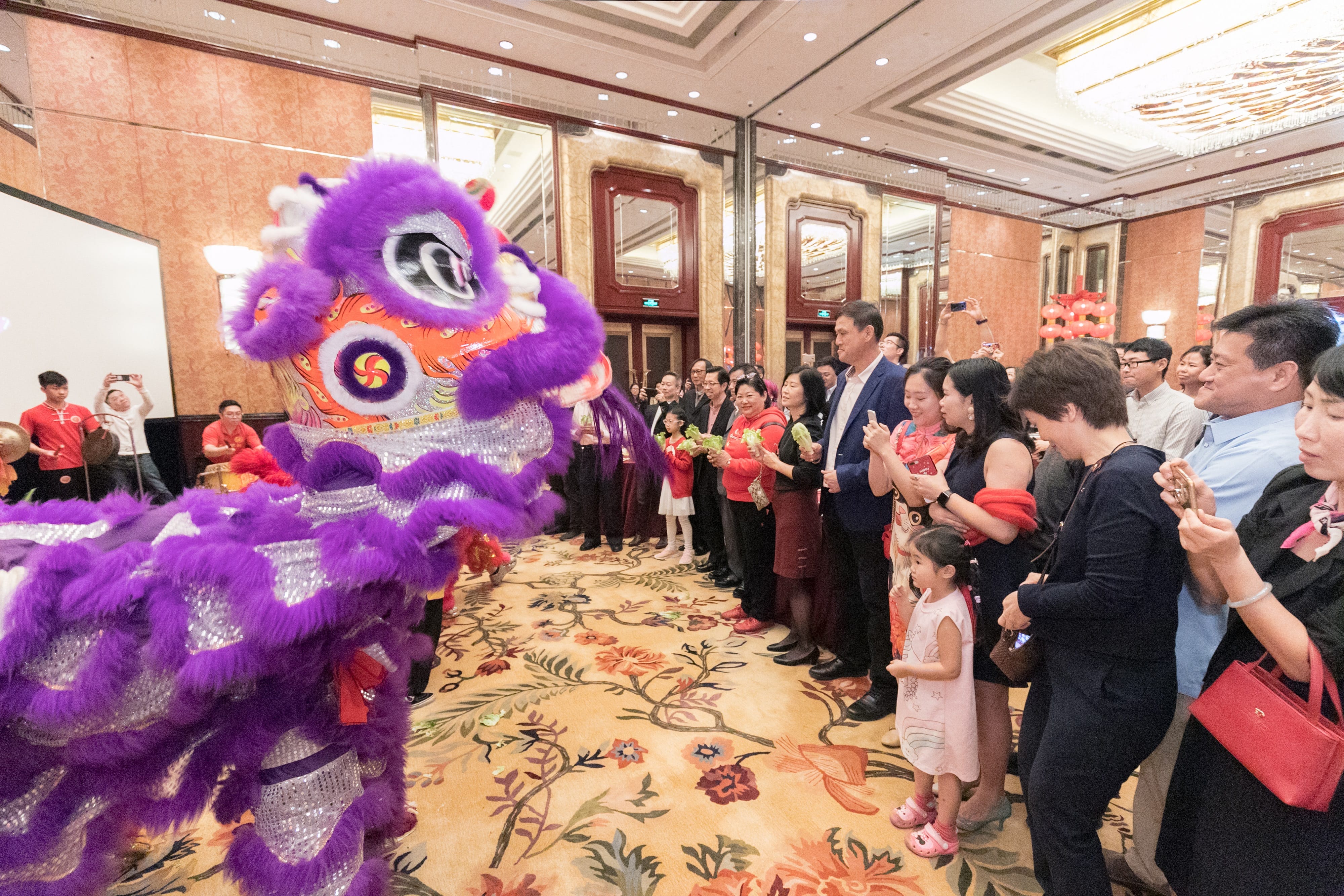 A purple Chinese lion dance entertains a crowd indoors.